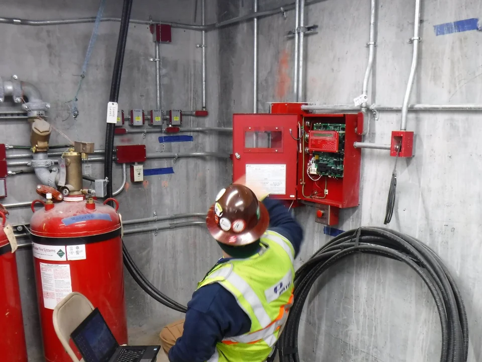 Technician testing a fire suppression release panel beside gas extinguishing cylinders